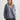 Woman wearing a gray sweater and dark pants against a white background