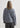 Person wearing a gray sweater and dark pants against a white background