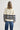 Person wearing a cream sweater with navy stripes and blue jeans on a white background