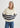 Woman wearing a cream sweater with navy stripes and blue jeans on a white background