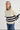 Woman wearing a cream sweater with navy stripes and blue jeans on a white background