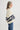Woman wearing a cream sweater with blue and black striped sleeves on a white background