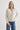 Woman wearing a beige cardigan and blue jeans on a white background