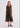 A woman modeling a sleeveless midi dress with a dark brown and black base featuring a vertical tribal-style pattern in rust red, olive green, and beige, paired with black strappy sandals against a plain white studio background.