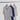 Three short-sleeve collared knit shirts hanging on wooden hangers from a metal rod against a white draped fabric backdrop. The shirts are in light gray, dark navy, and off-white.