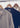 Three LAING knit polo shirts in gray, navy, and cream hanging on wooden hangers from a metal clothing rack.