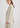 A woman wearing a light beige linen-blend blazer and matching trousers, photographed from the side against a clean white studio background.