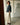 Woman in a black jacket and light pants standing in a minimalistic room.