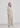 A woman modeling a light beige tailored suit consisting of a blazer and wide-leg trousers, standing against a draped white fabric backdrop.